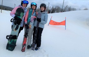 Kolme naista poseeraa lasketteluvarusteissa rinteessä