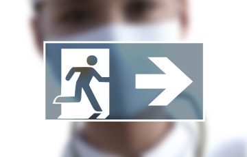 Exit-kyltti jonka takana epätarkat miehen kasvot, miehellä maski kasvoilla.