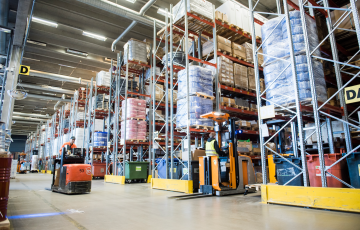 Mies ajaa trukkia korkeiden hyllyjen välissä isossa logistiikkakeskuksessa.