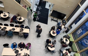 Ylhäältä parvelta katsottuna iso aulatila jossa pöytien ääressä kahvittelee ihmisiä.