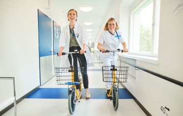 Kaksi terveysalan ammattilaista potkupyöräilemässä käytävässä, Kuva: Keski-Uudenmaan sote-TKIO -kuva Kuvaaja Iiro Rautiainen
