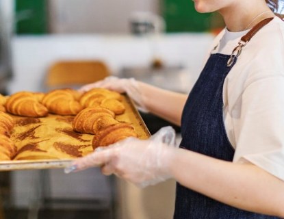 nainen laittaa croisantteja täynnä olevaa uunipeltiä kärryyn
