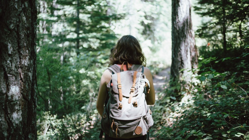 Nainen reppu selässä kävelemässä havumetsässä