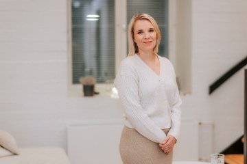 Puolivartalovalokuva jutussa esiintyvästä Sara Soinista. Sara seisoo valkoista seinää taustaa, ja katsoo kameraan. Sara hymyilee. Hänellä on päällään valkoinen neuletakki, ja beige hame. 